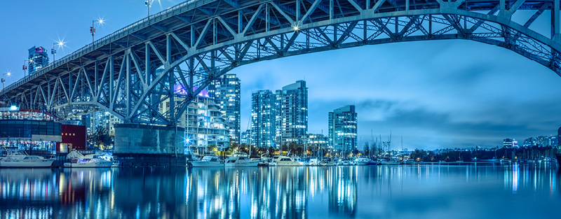Vancouver's Granville Island bridge at night with skyscrapers and marina with boats.