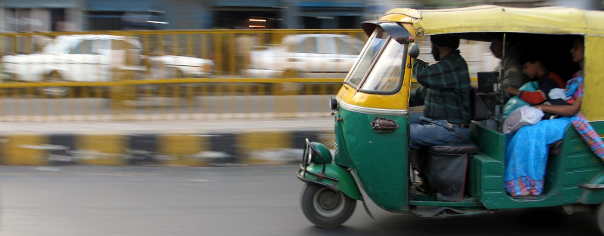 A green and yellow motorized rickshaw zips through the streets of Delhi, India