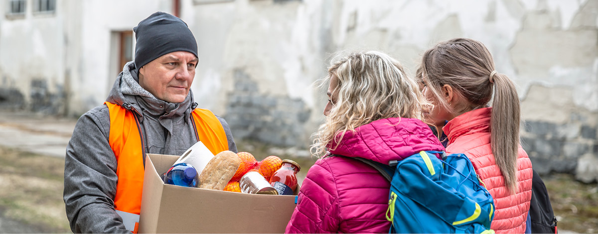 Volunteer in orange vest gives a box of food donation to fleeing refugees from Ukraine.