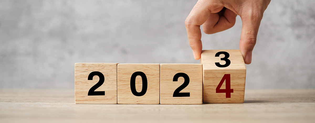 Hand flipping wooden blocks from 2023 to 2024, text on table.