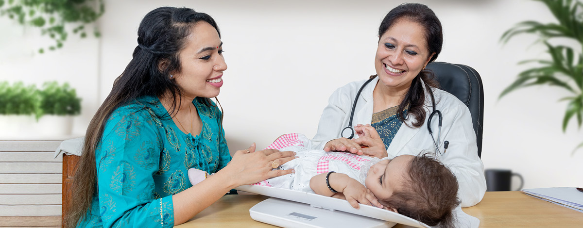 East Indian female pediatrician and mother measuring the weight of baby girl during a routine medical check-up.