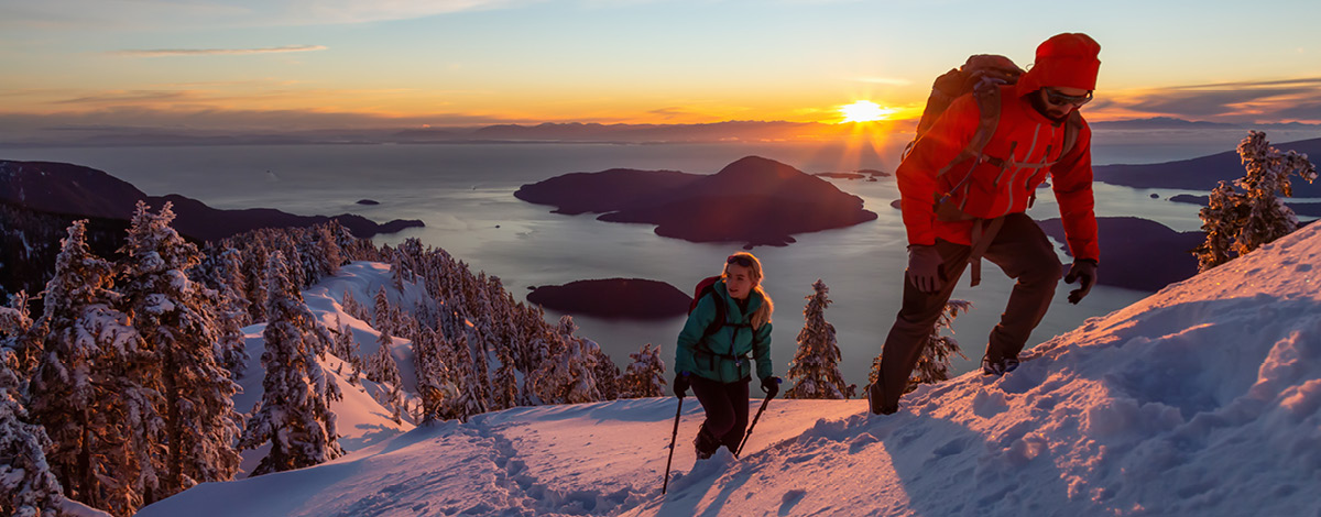 Deux personnes font de la randonnée au sommet d’une montagne pendant un coucher de soleil hivernal. Mount Harvey, North Vancouver, C.-B., Canada.