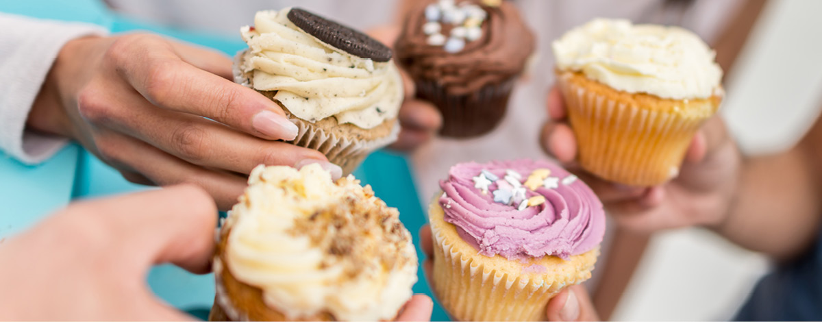 Group of people eating assorted cupcakes at a party.