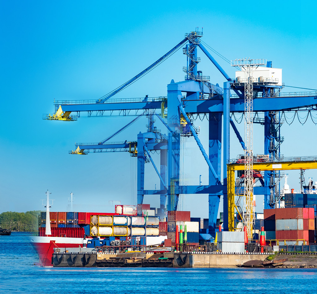Marine logistics hub. Containers ship in cargo port. Sea barge is awaiting unloading. Cargo cranes load containers onto ship. Transportation of goods by sea. Port on summer day. Oceanic logistics.