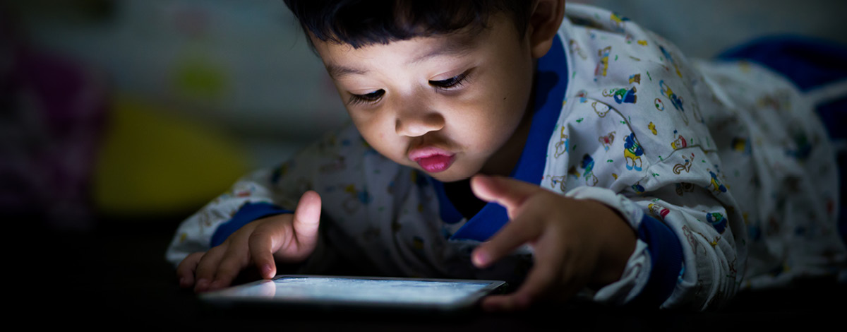 A little boy playing on a tablet at night.