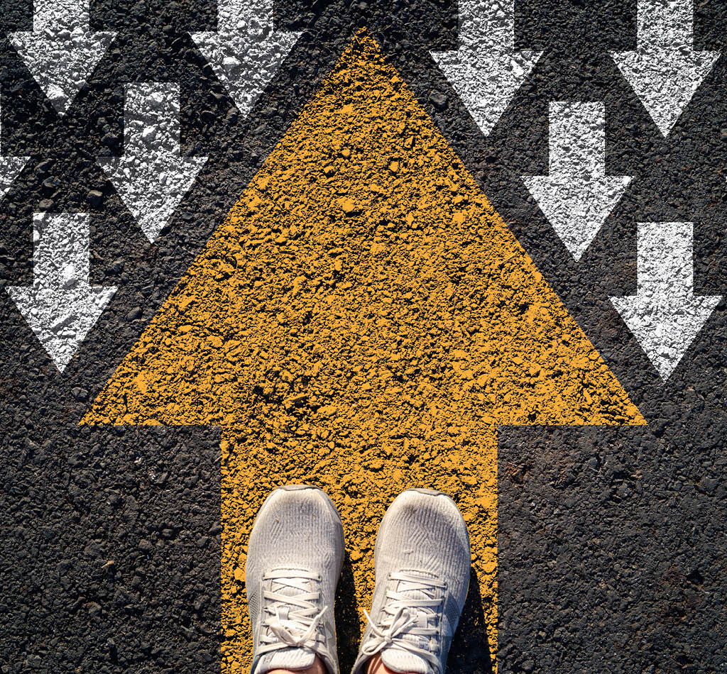 Vue de dessus de chaussures posées sur une flèche jaune vif pointant vers le haut, sur fond de flèches blanches pointant vers le bas.