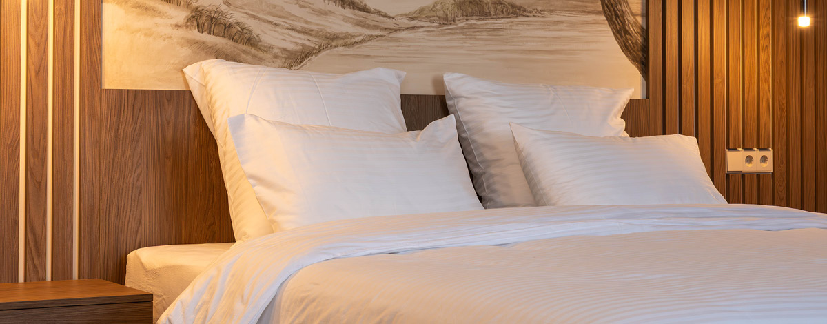 Cozy modern bedroom with white bedding, wood panel walls and warm lighting.