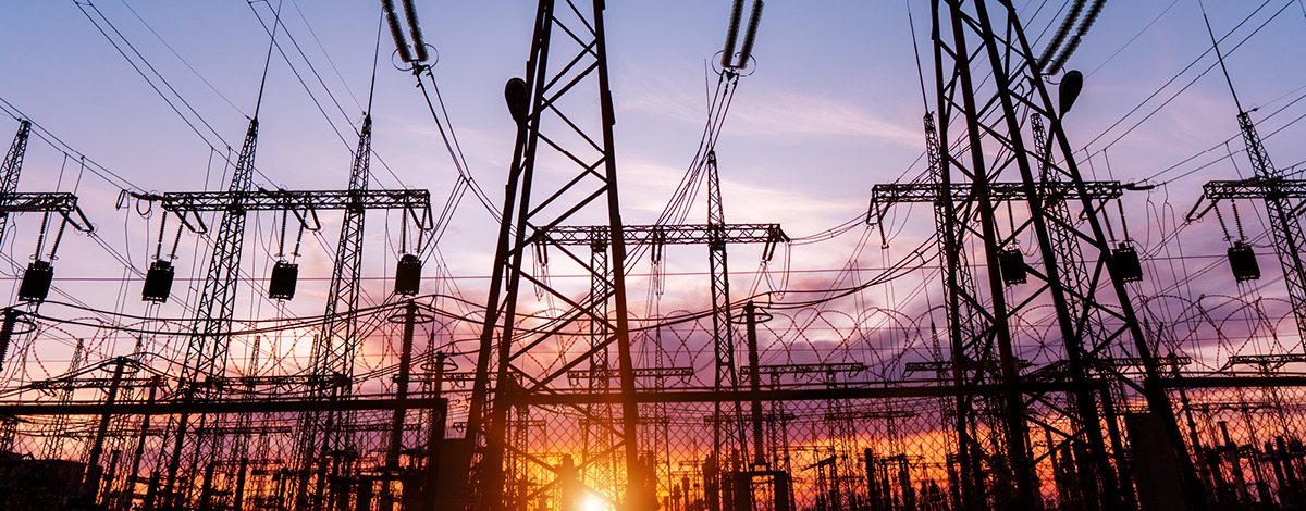 A silhouette of high voltage power lines against a colorful sky at sunrise.
