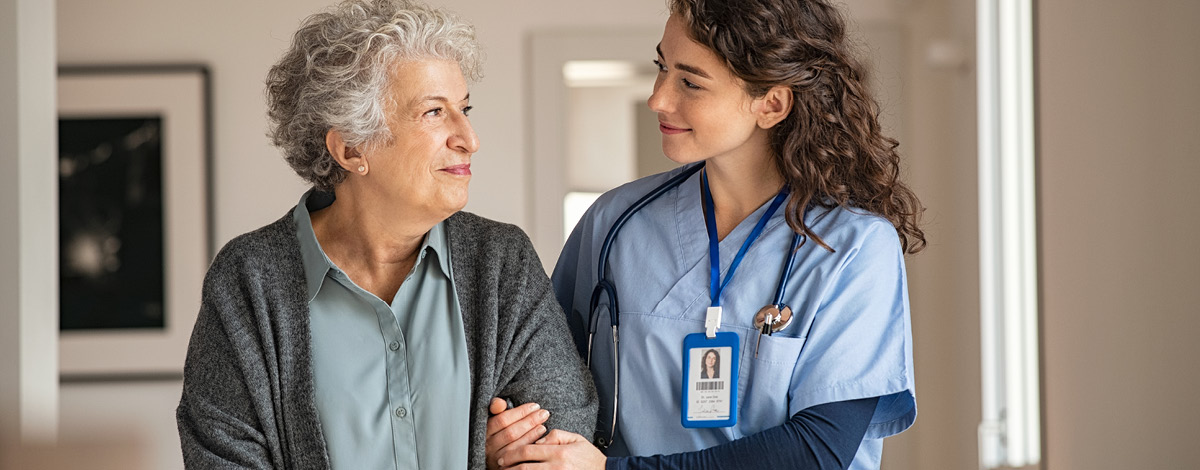 Caregiver assisting a senior woman, they're smiling at each other.