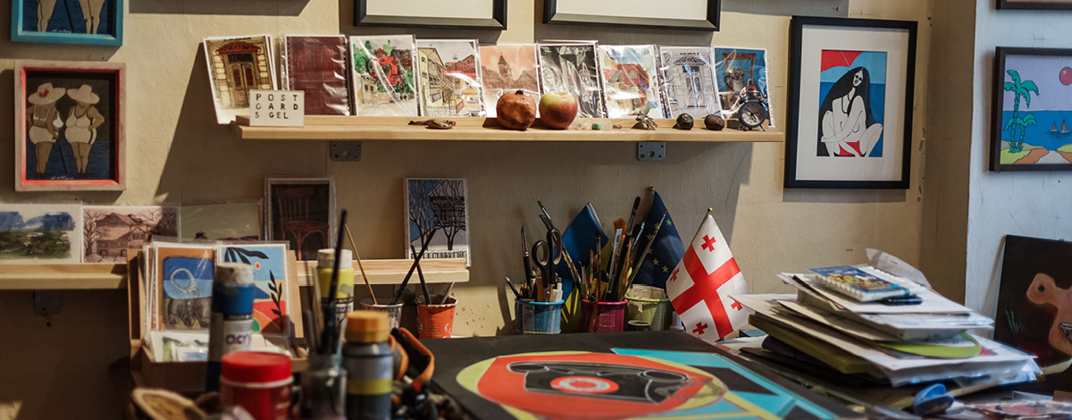 Artist studio in Tbilisi old town. Art-filled interior with supplies, handmade signs, posters & framed paintings.