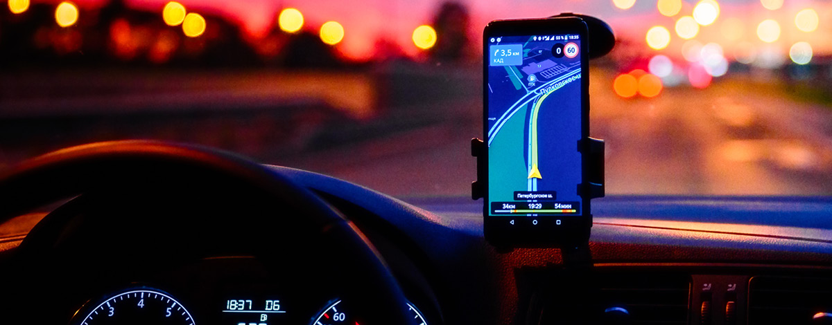 Smartphone displaying a map on a car dashboard at night. Dashboard and phone are in night mode.