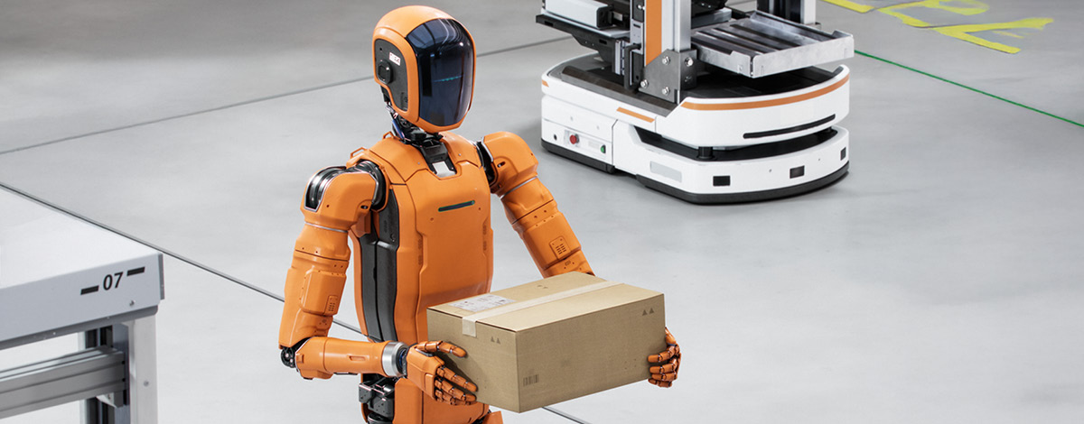 Autonomous humanoid robot holding a box at a distribution warehouse.