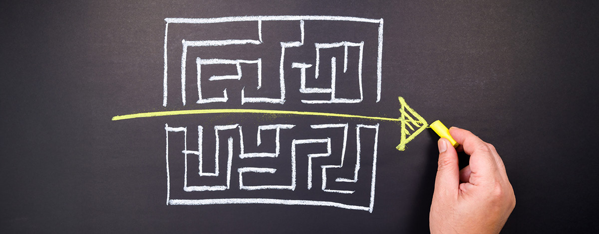 Chalk drawing of an arrow going straight through a complicated maze on a blackboard.